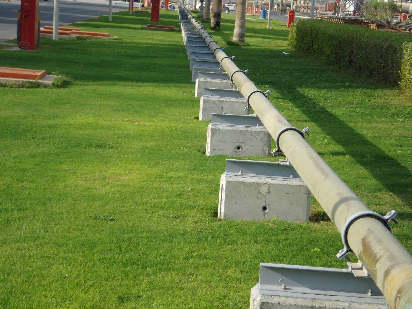 Above-ground potable water pipeline on concrete plinth supports across landscaped grounds at a DEWA site